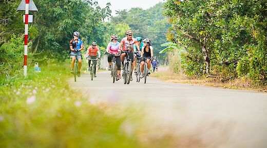 Cyclists riding along a rural road surrounded by greenery in Vietnam.