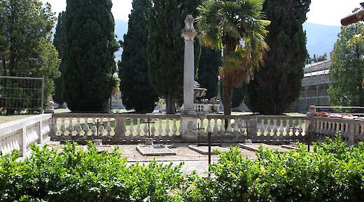 The garden area with a central stone column and railings, surrounded by tall cypress trees, located in Calci, Pisa, Italy.