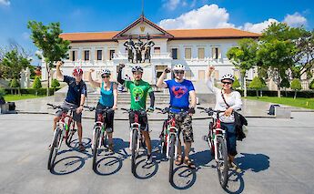 Cyclists wearing helmets stand with their bikes in front of the Three Kings Monument in Chiang Mai, Thailand.