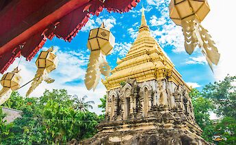A golden temple in Chiang Mai, Thailand, beneath a blue sky, with decorative lanterns hanging in the foreground.