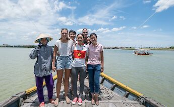 A group of people standing together on a boat in a wide river, with another boat visible in the background.