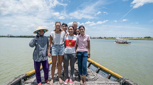 A group of people standing together on a boat in a wide river, with another boat visible in the background.