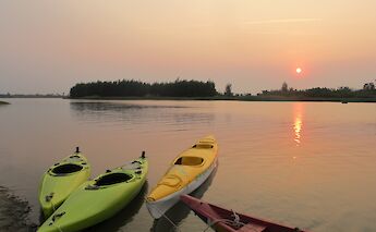 Kayaks docked on a calm body of water during a sunset in Hoi An, Vietnam, with the sun casting a warm glow on the scene.