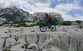 A person wearing a helmet bikes over large white rocks with rugged mountains in the background in Grabovica, Zabljak, Montenegro.