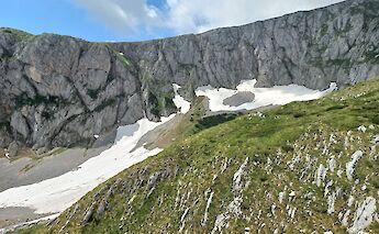 A rugged mountain landscape with patches of snow beneath a clear blue sky.