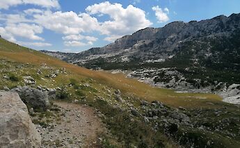 A rocky landscape with grass and rugged hills under a partly cloudy sky, in Grabovica, Zabljak, Montenegro.