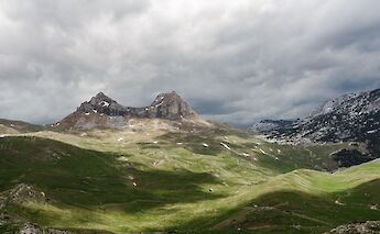 Mountainous landscape with grassy hills and dramatic clouds overhead.