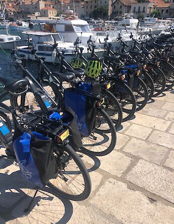Row of bicycles with blue saddle bags lined up along a waterfront in a Croatian port.