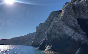 View of rocky coastal cliffs and a cave opening in northern Dalmatia, Croatia, with the sun shining brightly above.