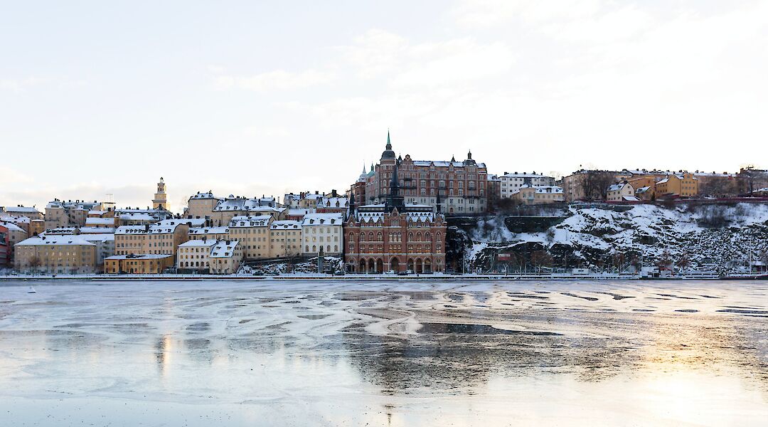 View of snow-covered buildings along the waterfront in Södermalm, Stockholm, under a clear sky.