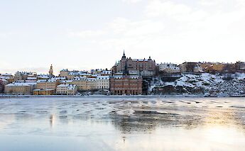 View of snow-covered buildings along the waterfront in Södermalm, Stockholm, under a clear sky.