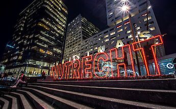 A night scene in Utrecht, Netherlands, featuring illuminated buildings and holiday-themed light decorations.