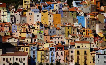 A cluster of colorful, tightly packed buildings on a hillside, showcasing vibrant architecture in Sardinia, Italy.