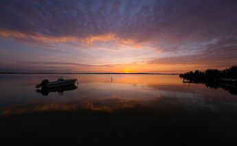 A tranquil scene of a boat on calm waters during a vibrant sunset in Cabras, Sardinia, Italy.