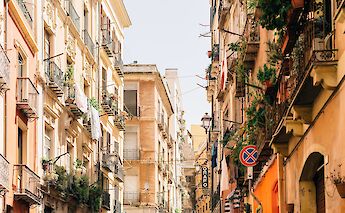 A narrow street in Cagliari, Sardinia, lined with colorful buildings and balconies adorned with plants and laundry.