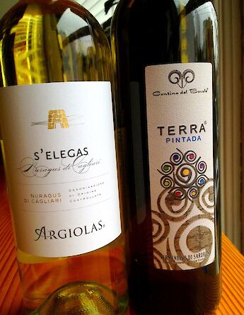 Two wine bottles from Sardinia, Italy, displayed on a wooden surface.