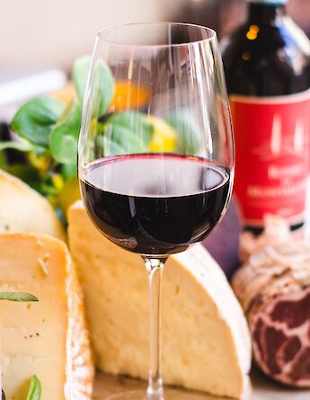 A close-up of a glass of red wine next to a selection of Italian cheeses and charcuterie.