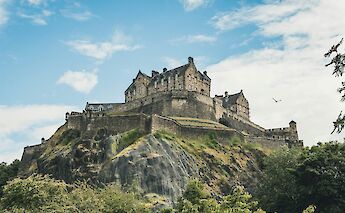 Edinburgh Castle on a rocky hill, with a blue sky and some clouds in the background.