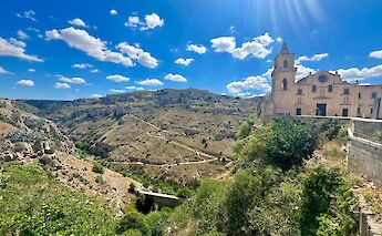 A scenic view of Murgia National Park with a church on the hillside under a bright blue sky.