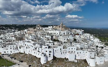 An aerial view of Ostuni, showcasing the town's characteristic white buildings under a partly cloudy sky.