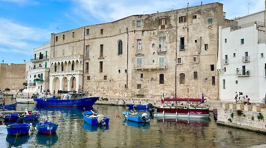 Fishing boats moored in the waters of Porto Antico di Monopoli, with historic stone buildings on the shore.