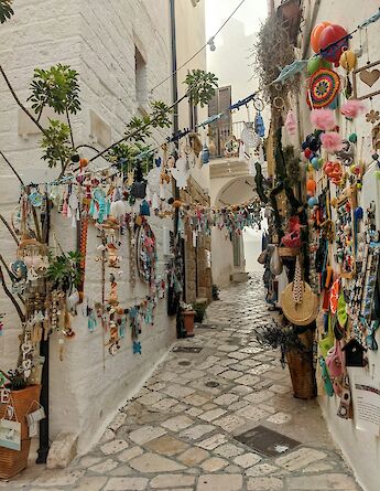 A narrow street in Polignano a Mare, lined with colorful hanging decorations and souvenirs.