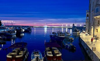 A vibrant sunset over the harbor in Monopoli, with boats docked along the waterfront.