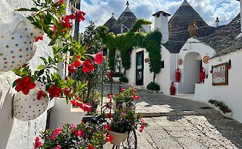 A picturesque street in Alberobello, featuring traditional trulli houses with conical roofs and vibrant flowers.