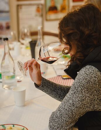 A person sampling red wine at a table set with water bottles and a plate of sliced cheese and salami.