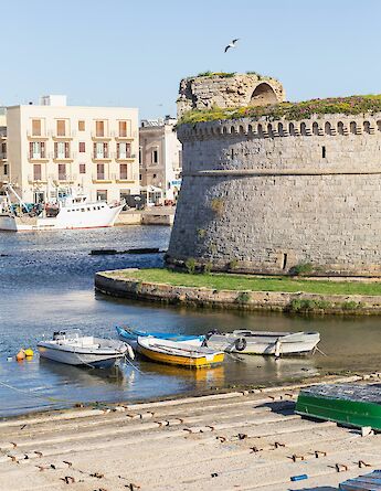 Gallipoli's picturesque harbor with boats docked alongside a stone structure and buildings in the background.