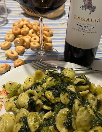 A plate of orecchiette with greens served alongside a glass of red wine and traditional Puglian snacks.