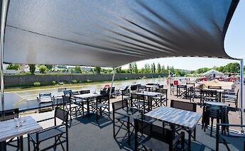 A shaded outdoor dining area on the deck of a boat with tables and chairs overlooking a river and&hellip;
