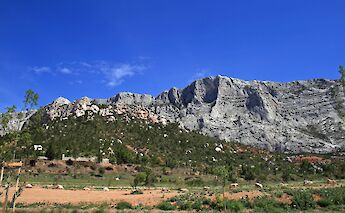 -  
-  
-  
-  
- Rocky landscape of Montagne Sainte-Victoire with scattered vegetation and a cross visible at the peak under a pale sky.