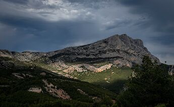 Montagne Sainte-Victoire in Aix-en-Provence, France, dramatically lit against a cloudy sky with a forested landscape below.