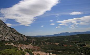 View from Montagne Sainte-Victoire in Aix-en-Provence, France, showcasing rugged cliffs, expansive greenery, and a distant horizon under a sky with scattered clouds.
