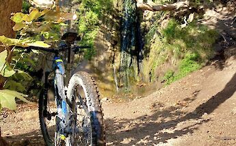 A mountain bike parked near a waterfall, surrounded by rocky terrain and greenery.