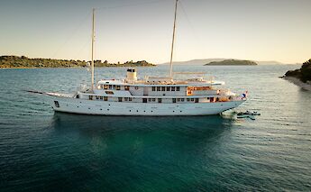 A white yacht named Bellezza with two masts is anchored in a calm body of water, surrounded by&hellip;