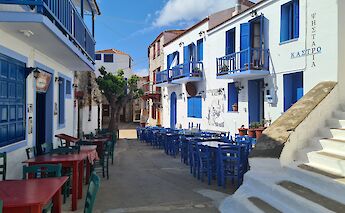 Narrow cobbled streets lined with whitewashed houses and blue shutters in Chora, Alonissos, with outdoor seating.