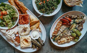 Plates of traditional Greek food, including salads, grilled vegetables, dips, and stuffed pastries.