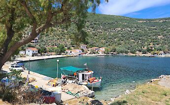 A small fishing boat docked at Kottes Port, surrounded by traditional houses and hilly green landscape in Pelion, Greece.