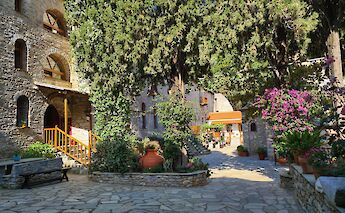 The courtyard of the Monastery of Evangelistria, with stone buildings, trees, and colorful flowers in Sporades Islands, Greece.