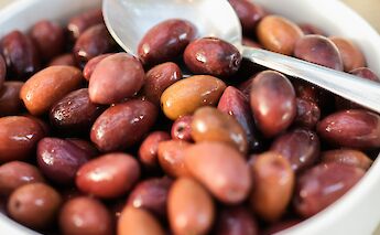 A close-up of a bowl filled with a variety of olives, with a spoon resting on top.