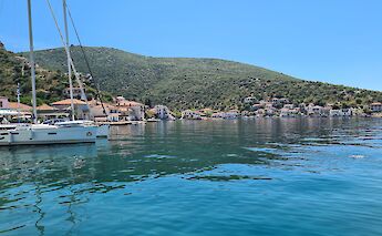 Agia Kyriaki Port in Pelion, Greece, with calm waters, sailboats, and buildings surrounded by green hills.
