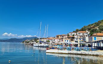 A coastal view of Agia Kyriaki, a charming fishing village on the Pelion Peninsula, featuring boats docked in the harbor and traditional buildings along the waterfront.