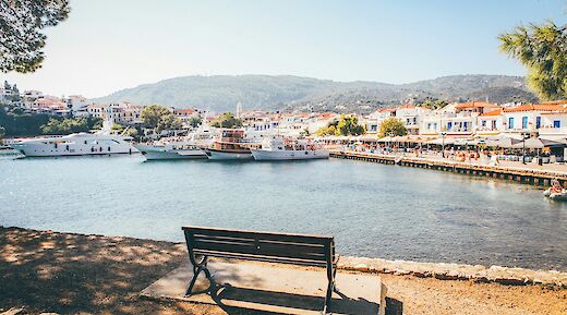 Skiathos Beach in Greece, showing a waterfront with parked boats and colorful buildings in the background.