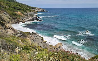 Perivoliou Beach on Skopelos Island, Greece, showing a rugged coastline with clear blue water and greenery.