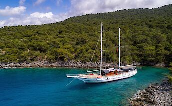 A sailboat named Milo M is anchored in a secluded cove with clear turquoise water, surrounded by…