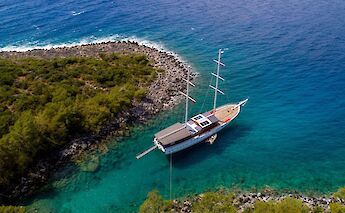 Aerial view of the Milo M, a boat anchored in turquoise waters near a rocky coast with dense green&hellip;