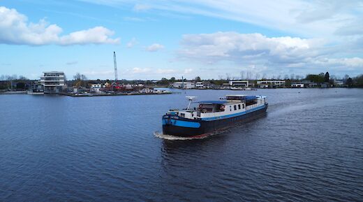 The boat "La Mar" is navigating through a waterway with buildings and a crane visible on the shore.