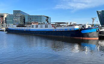 La Mar boat docked beside modern buildings with a blue sky above.